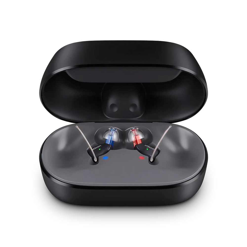 A pair of Oticon Zeal™ 1 small in-ear hearing aids, one with a blue mark and one with a red mark, are displayed inside an open black charging case on a white background.